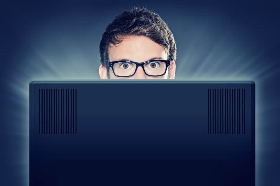 Web designer with glasses peeking from behind a computer screen